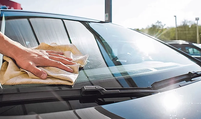 Pessoa lavando carro com espuma e mangueira, carro limpo e brilhante.