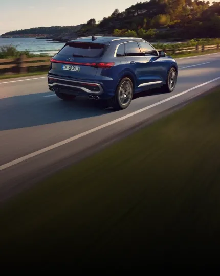 Audi SQ5 azul em movimento em estrada à beira-mar, visto de trás