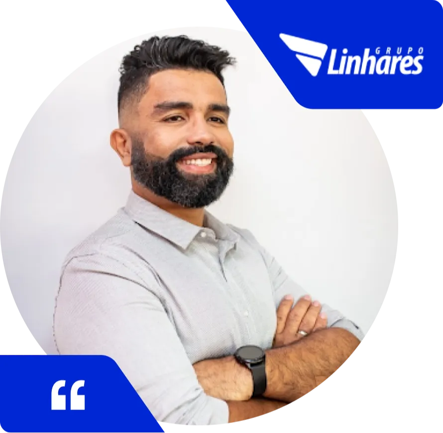 Homem sorridente com barba e cabelo escuro, vestindo camisa social clara e relógio preto, posando com os braços cruzados em frente a um fundo branco. No canto superior direito, há o logotipo do Grupo Linhares em azul, e no canto inferior esquerdo, um ícone de aspas indicando depoimento.