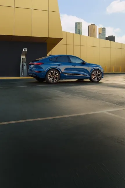 Audi e-tron Sportback azul conectado a um carregador elétrico junto a uma parede amarela