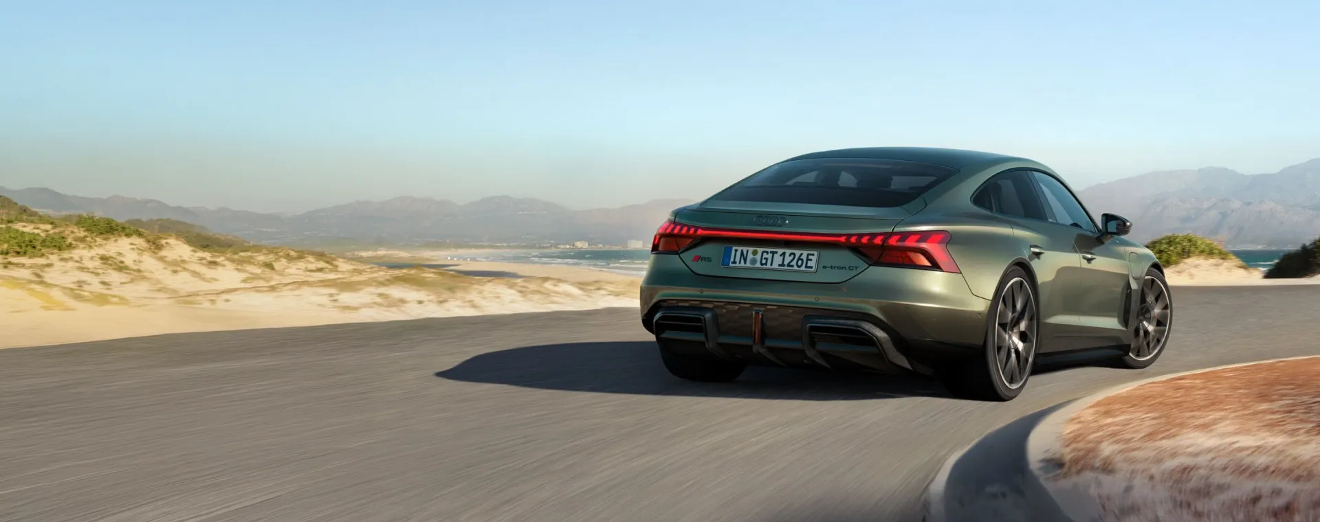 Audi RS e-tron GT verde em movimento em estrada litorânea, visto de trás