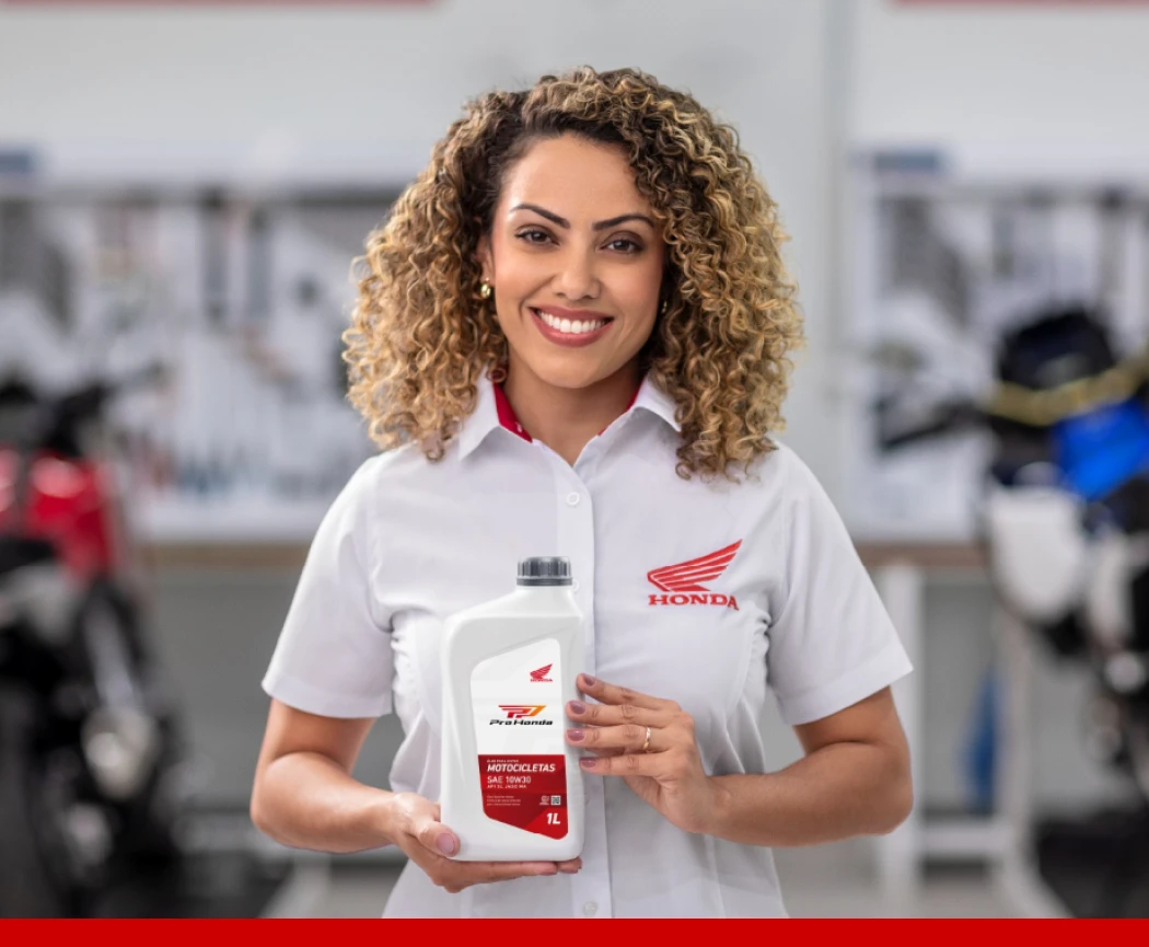 Funcionária da Honda sorrindo em uma oficina, segurando um frasco de óleo para motocicletas da marca.