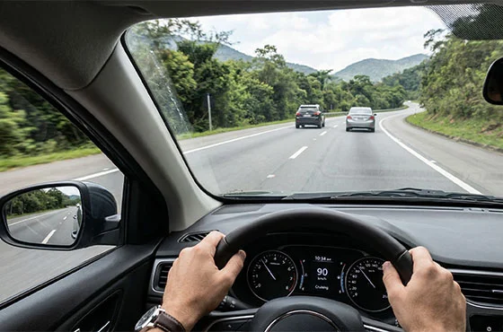 Motorista dirigindo carro em rodovia, focando na segurança.