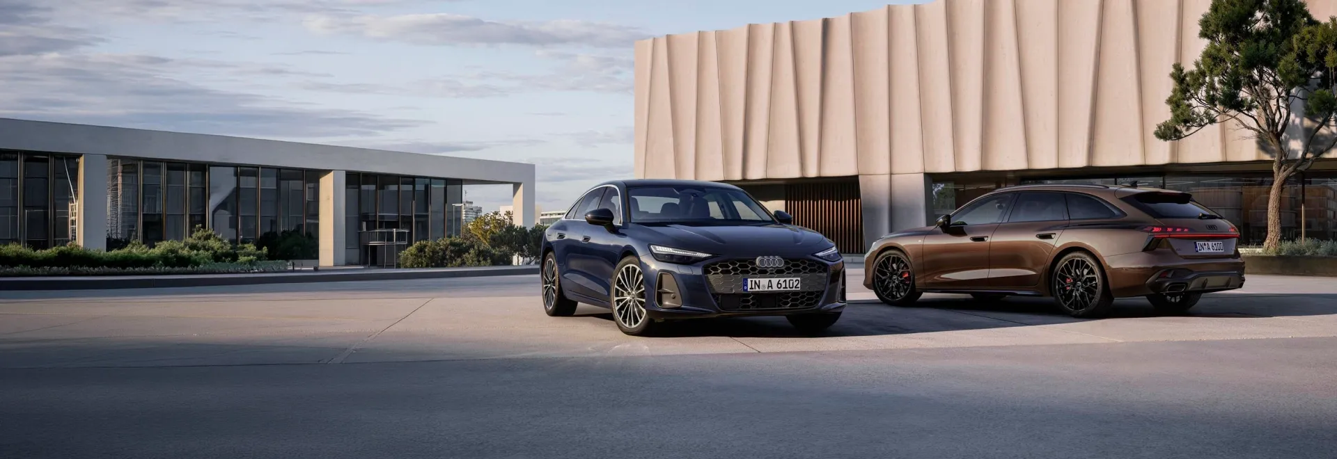 Audi A6 azul-escuro e Audi A6 Avant marrom estacionados diante de um edifício moderno