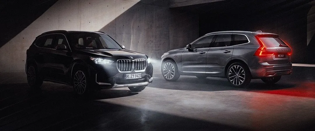 BMW preto e Volvo cinza em garagem de concreto, com os faróis acesos