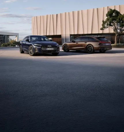 Audi A6 azul-escuro e Audi A6 Avant marrom estacionados diante de um edifício moderno
