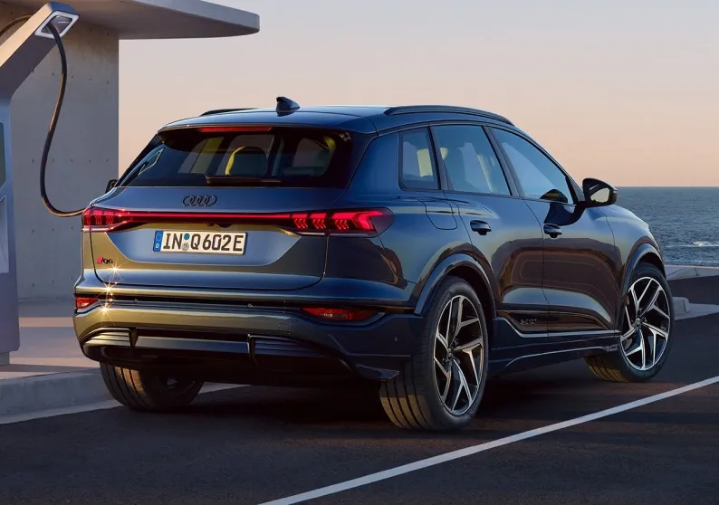 Audi Q6 e-tron cinza conectado a um carregador elétrico à beira-mar, visto de trás