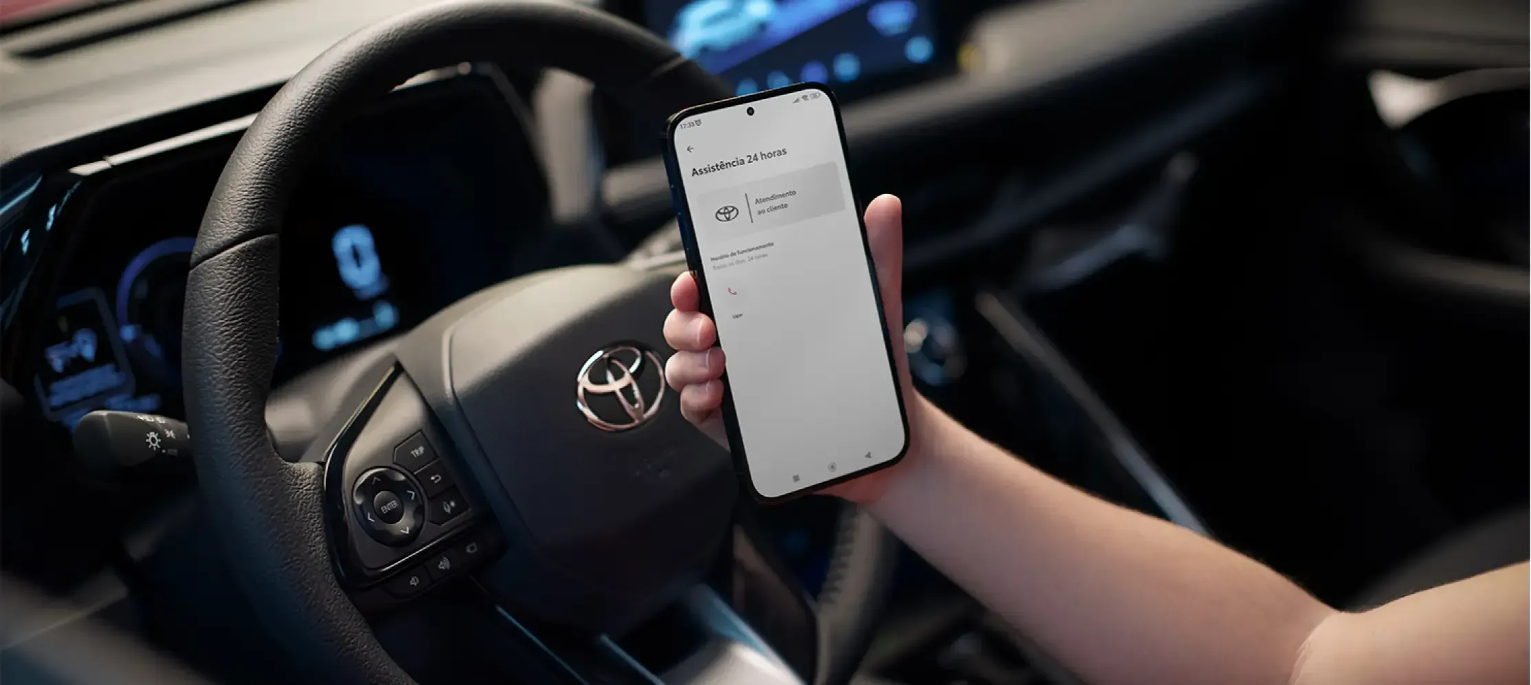 Mão segurando um telefone próximo ao volante Toyota.