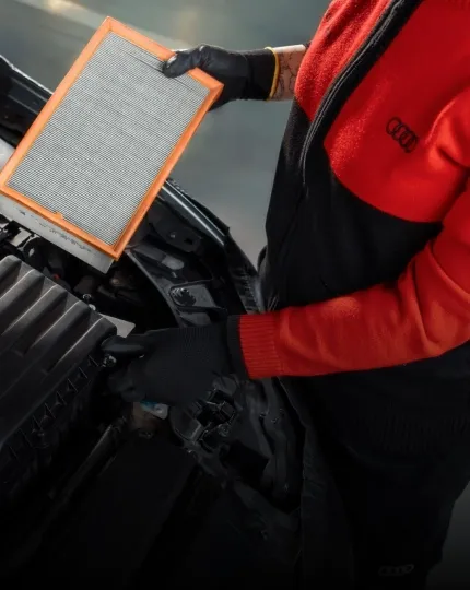 Técnico de uniforme Audi segurando um filtro de ar sobre o motor de um veículo
