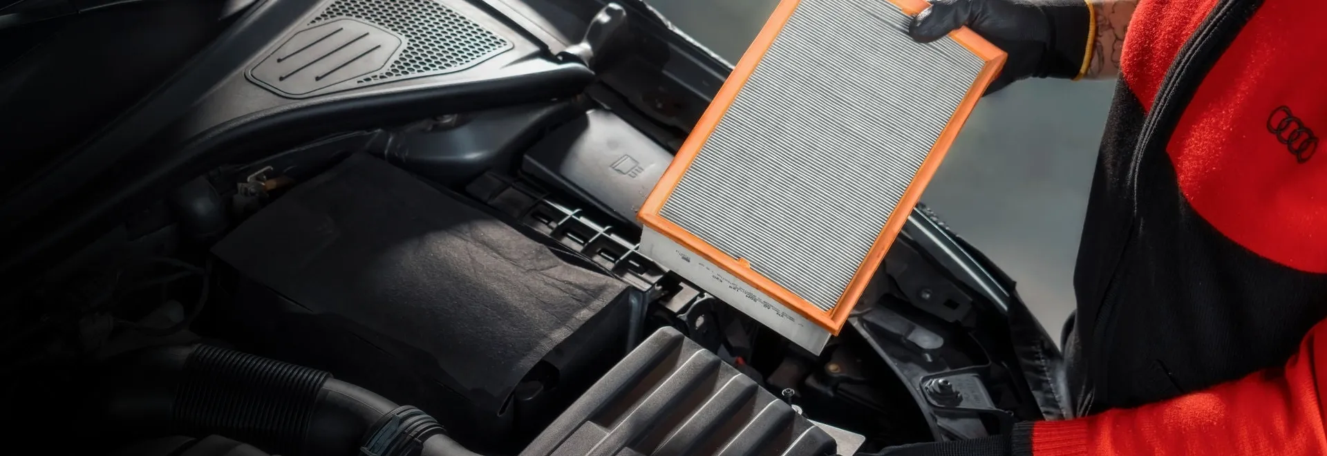 Técnico de uniforme Audi segurando um filtro de ar sobre o motor de um veículo