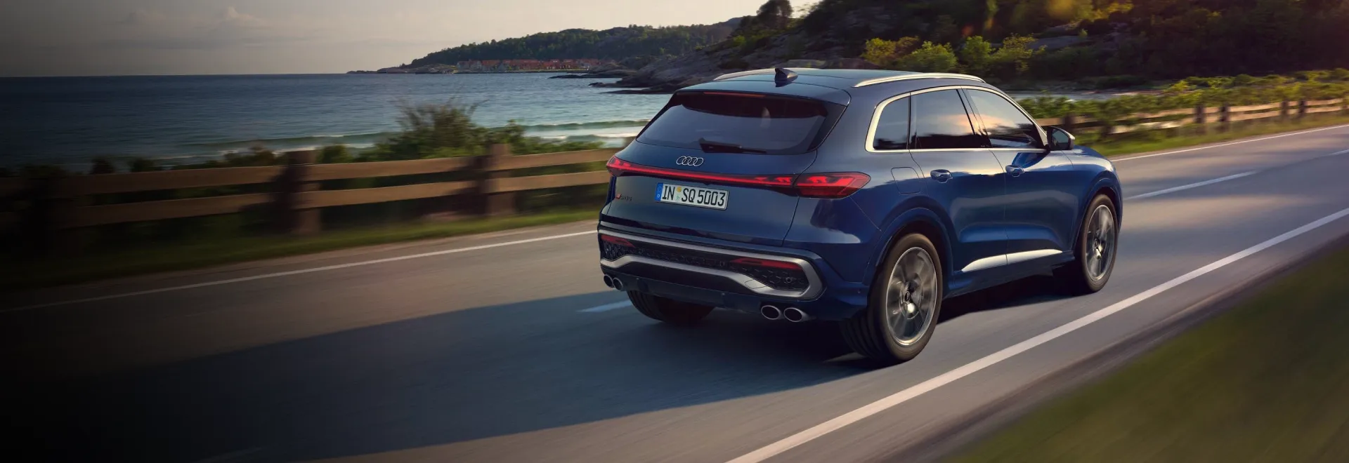 Audi SQ5 azul em movimento em estrada à beira-mar, visto de trás