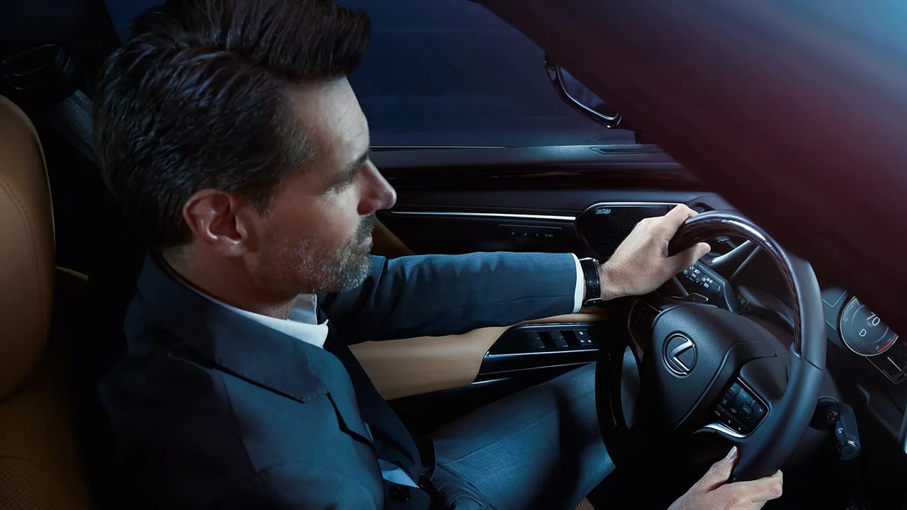 Motorista de terno ao volante de um sedã Lexus, com a cabine em tons escuros