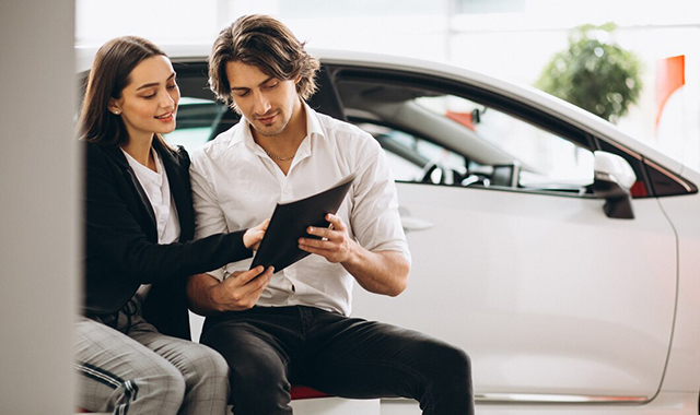 Homem e mulher felizes ao lado de um carro e uma moto novos.