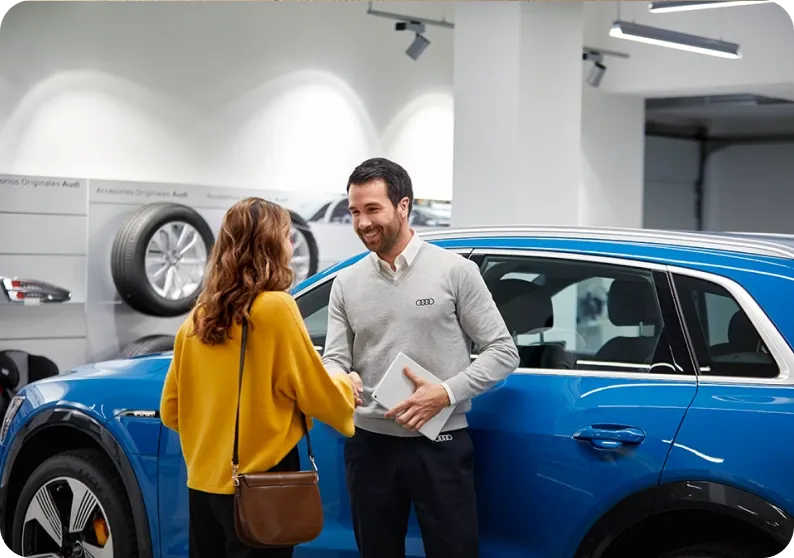 Consultor Audi cumprimentando uma cliente ao lado de um Audi e-tron azul no showroom