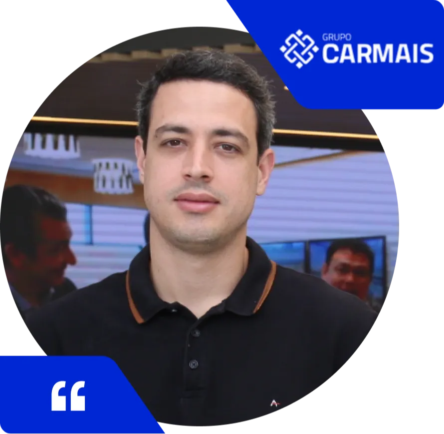 Homem de expressão neutra, cabelo curto escuro, vestindo camisa polo preta com detalhes marrons, posando em um ambiente interno com outras pessoas ao fundo. No canto superior direito está o logotipo do Grupo Carmais em azul, e no canto inferior esquerdo, um ícone de aspas indicando depoimento.