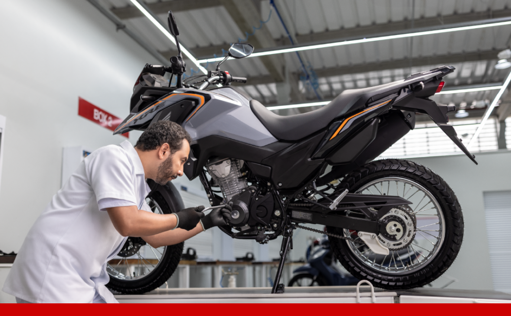 Mecânico da Honda realizando manutenção em uma motocicleta em uma oficina, ajustando componentes do motor.