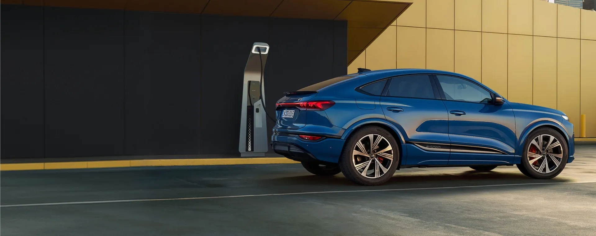 Audi e-tron Sportback azul conectado a um carregador elétrico junto a uma parede amarela