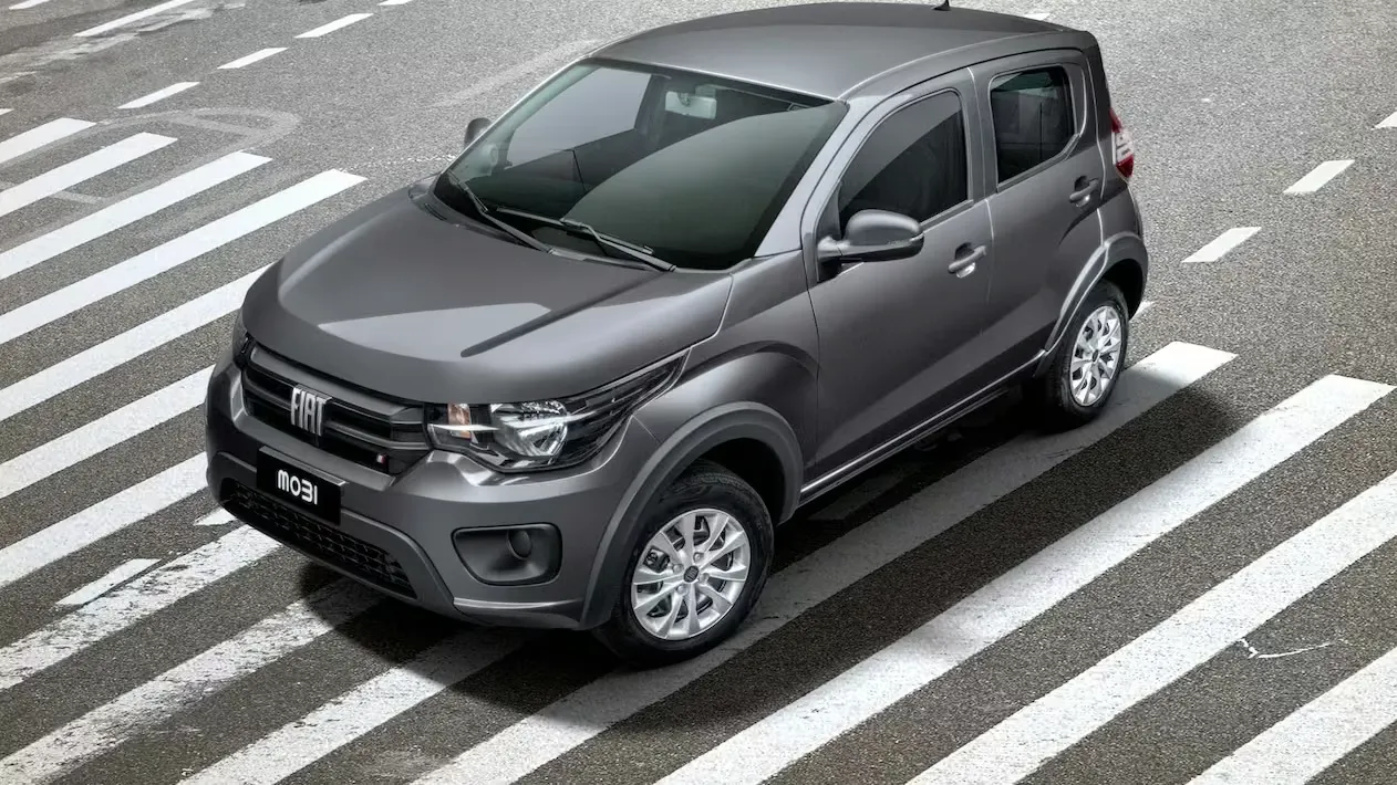 Fiat Mobi cinza visto em ângulo 3/4 frontal, parado sobre faixa de pedestres em ambiente urbano.