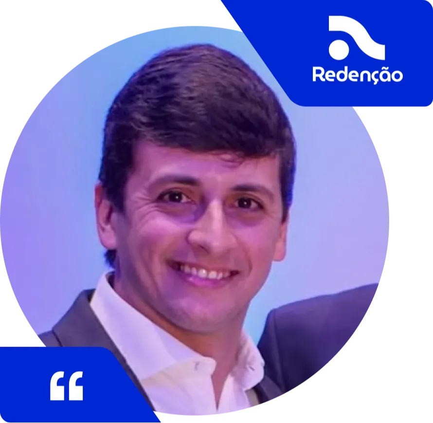 Homem sorridente de cabelos castanhos escuros, vestindo camisa branca e blazer escuro, posando diante de um fundo azul. No canto superior direito da imagem está o logotipo da Redenção em azul, e no canto inferior esquerdo, o ícone de aspas indicando depoimento.